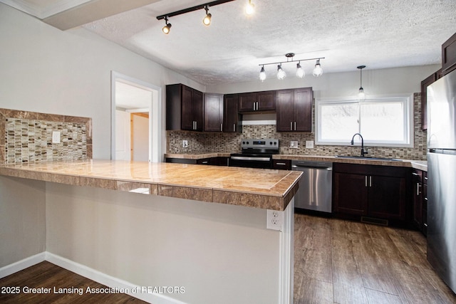 kitchen with wood finished floors, a peninsula, a sink, stainless steel appliances, and dark brown cabinets