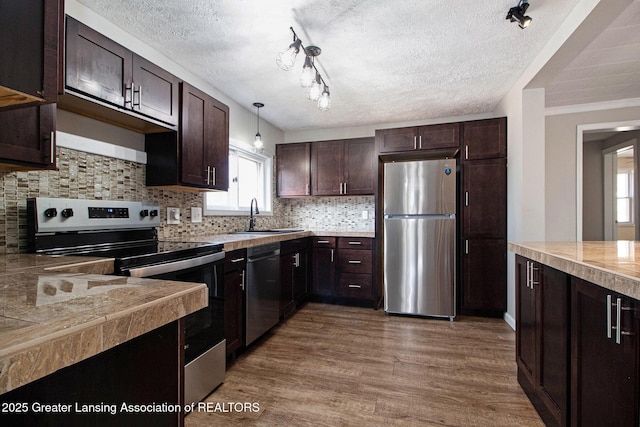 kitchen with backsplash, dark brown cabinets, wood finished floors, stainless steel appliances, and a sink