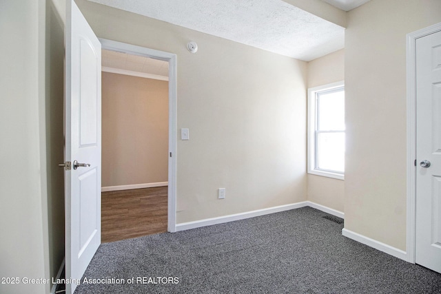 unfurnished bedroom featuring visible vents, baseboards, dark carpet, and a textured ceiling