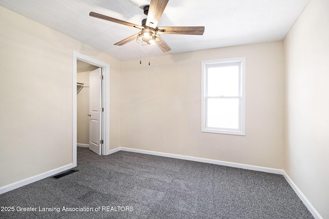 unfurnished bedroom with a walk in closet, carpet flooring, baseboards, and visible vents