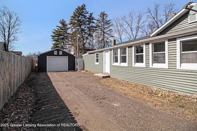 view of side of home with a detached garage, fence, a chimney, an outdoor structure, and driveway