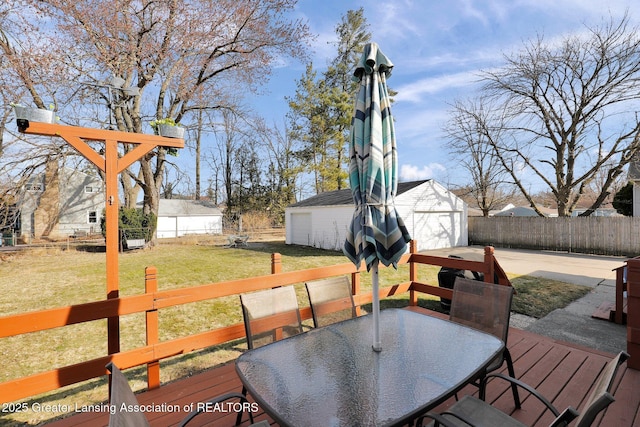 wooden terrace with a detached garage, a lawn, outdoor dining area, a fenced backyard, and an outbuilding