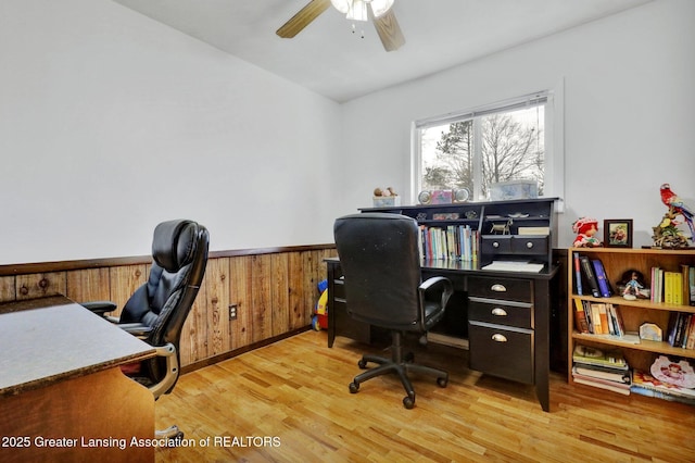 office space with wainscoting, wood walls, light wood-type flooring, and a ceiling fan