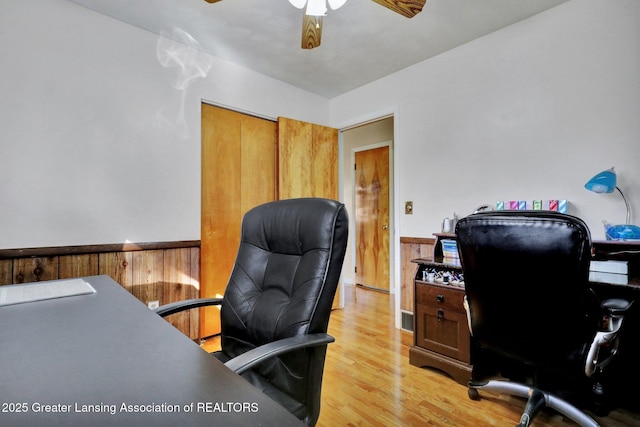 office space with light wood-style flooring, wooden walls, ceiling fan, and wainscoting