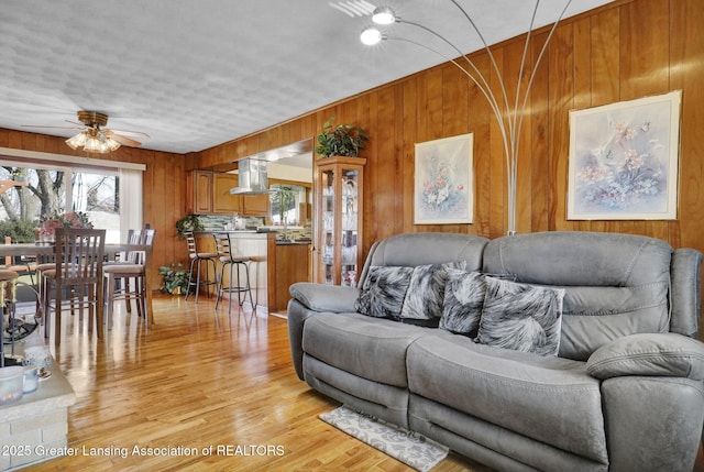 living area featuring light wood-type flooring, wood walls, and a ceiling fan