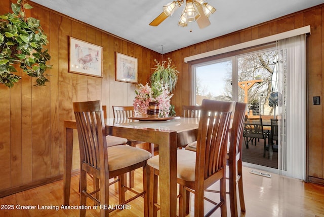 dining space with visible vents, wood walls, a ceiling fan, and wood finished floors