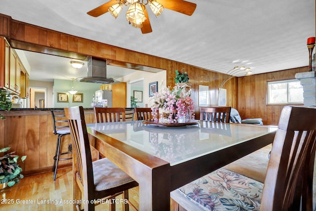 dining room featuring wood finished floors, a ceiling fan, and wood walls