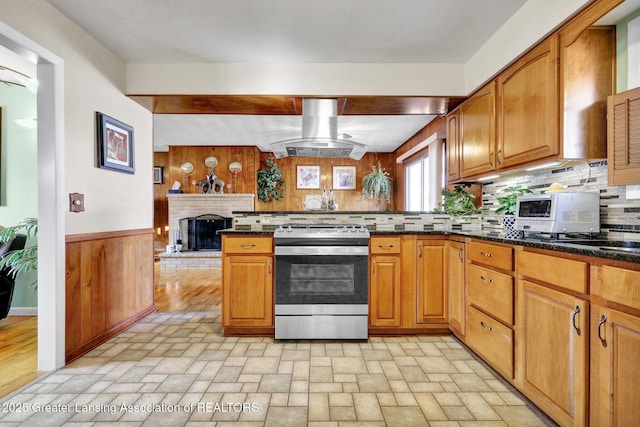 kitchen with backsplash, stainless steel range with gas cooktop, wood walls, a peninsula, and island exhaust hood