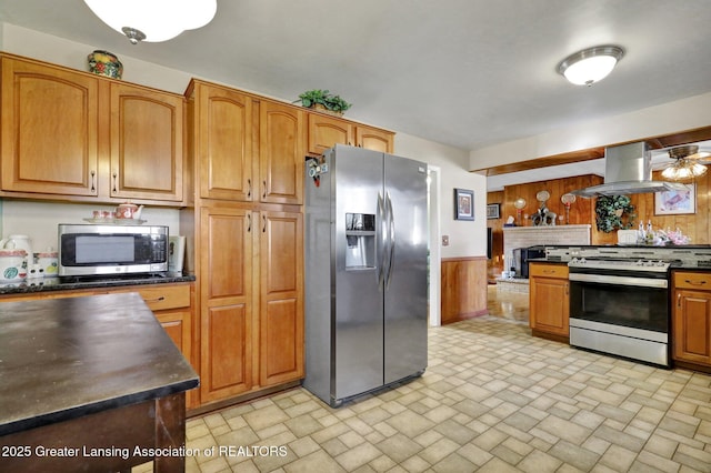 kitchen featuring dark countertops, ventilation hood, wood walls, wainscoting, and stainless steel appliances