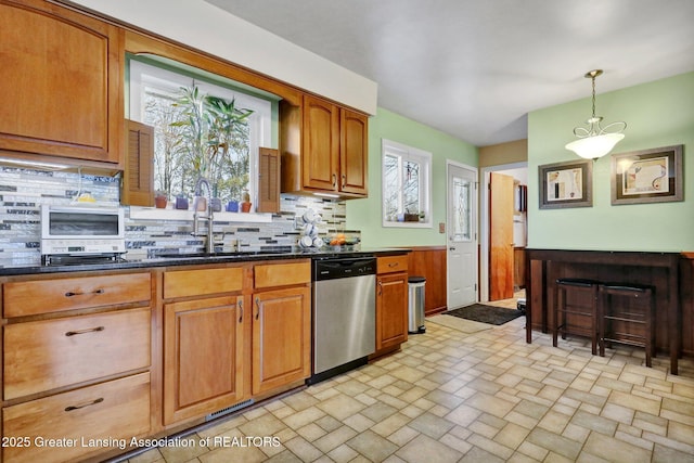 kitchen with decorative light fixtures, stone finish flooring, tasteful backsplash, stainless steel dishwasher, and brown cabinetry