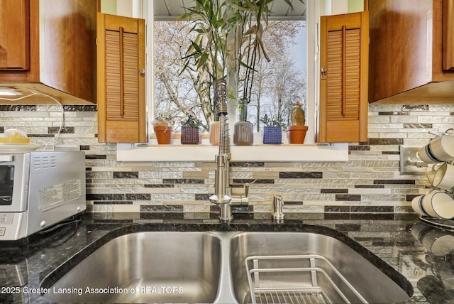 details featuring brown cabinetry, decorative backsplash, dark stone counters, and extractor fan