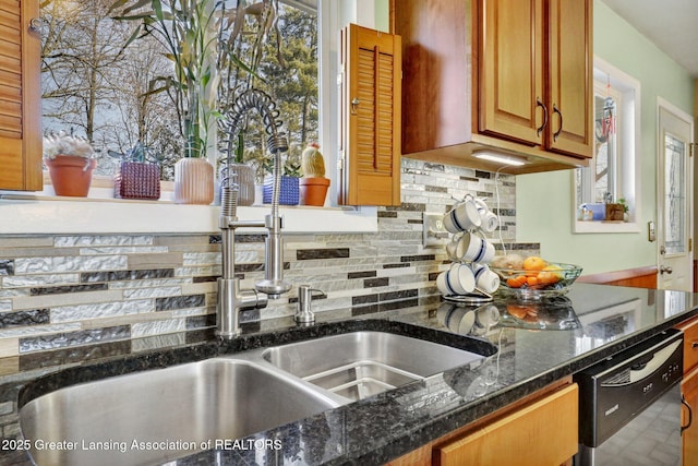 kitchen with brown cabinets, dark stone countertops, a sink, decorative backsplash, and dishwasher