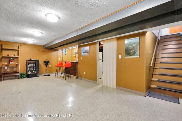 finished below grade area with stairway, a textured ceiling, freestanding refrigerator, and baseboards