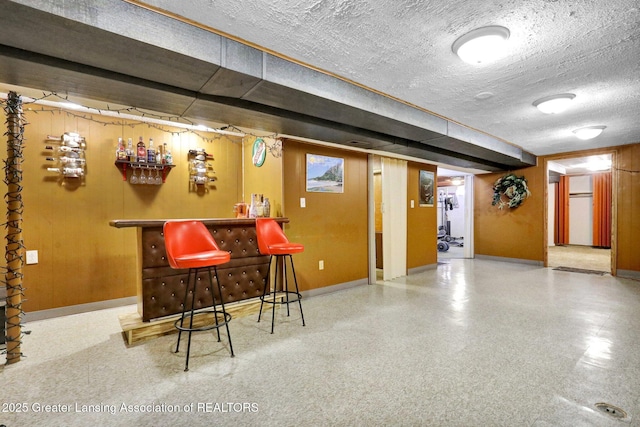 bar featuring a dry bar, a textured ceiling, speckled floor, and baseboards