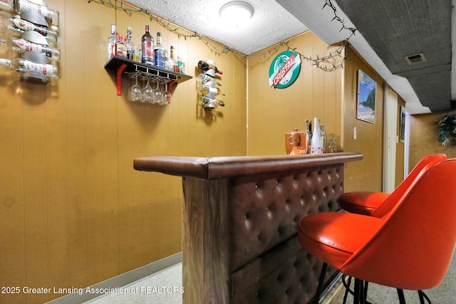 bar featuring visible vents, a textured ceiling, a bar, and baseboards