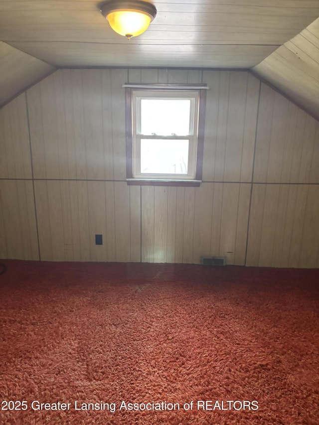 bonus room featuring visible vents, carpet, wooden walls, and vaulted ceiling