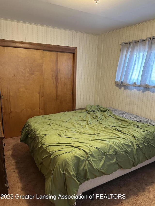 bedroom with wallpapered walls, carpet, and a closet