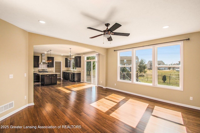 unfurnished living room with visible vents, arched walkways, dark wood-style flooring, and baseboards