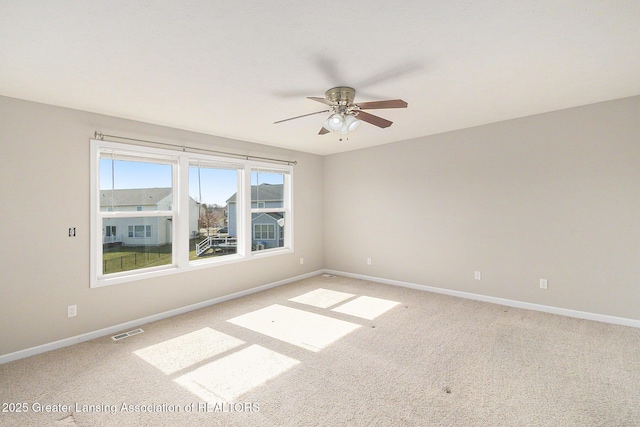 spare room featuring light colored carpet, a ceiling fan, visible vents, and baseboards