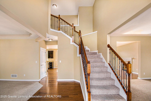 stairway with visible vents, a high ceiling, baseboards, and wood finished floors