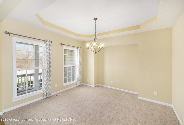 spare room with a tray ceiling, a notable chandelier, baseboards, and visible vents