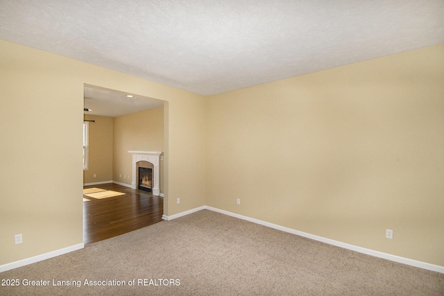 unfurnished living room featuring a fireplace with flush hearth, a textured ceiling, and baseboards