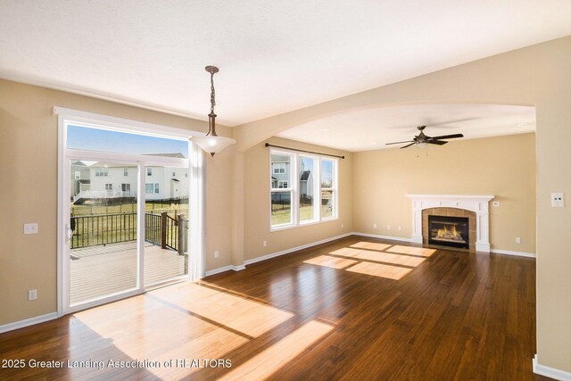 unfurnished living room featuring a fireplace, wood finished floors, baseboards, and ceiling fan