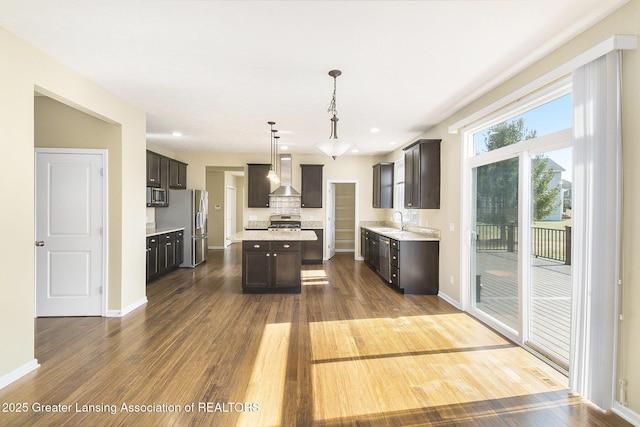 kitchen featuring a sink, light countertops, dark wood-type flooring, appliances with stainless steel finishes, and wall chimney exhaust hood