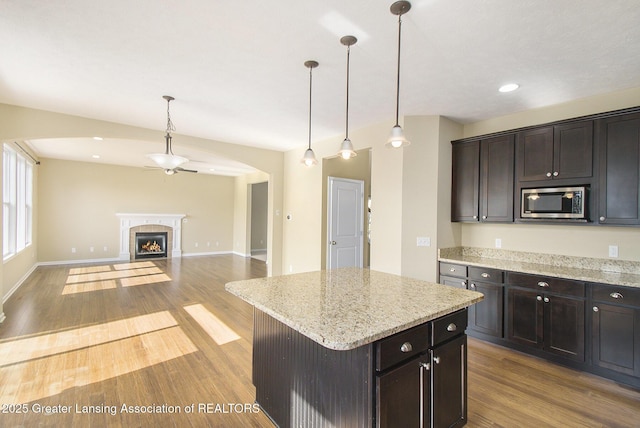 kitchen with stainless steel microwave, wood finished floors, a lit fireplace, baseboards, and hanging light fixtures