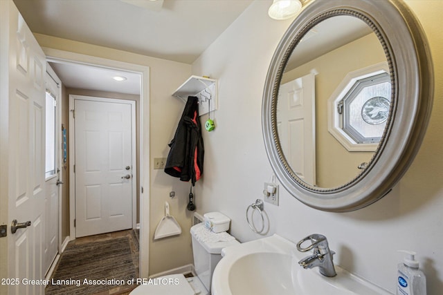 half bathroom featuring wood finished floors, toilet, baseboards, and a sink