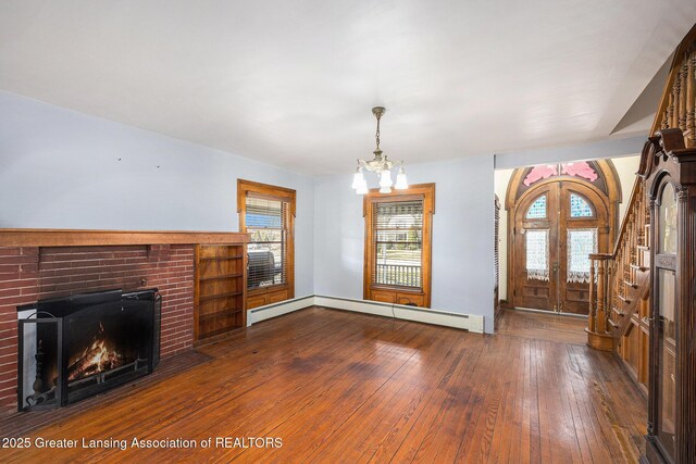 unfurnished living room featuring hardwood / wood-style flooring, a fireplace, a baseboard radiator, a chandelier, and stairs