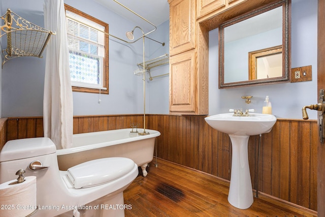 full bathroom with a wainscoted wall, toilet, wood finished floors, wood walls, and shower / bath combination with curtain
