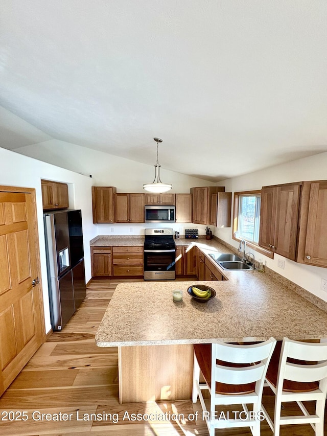 kitchen featuring vaulted ceiling, light wood-style flooring, a peninsula, stainless steel appliances, and a sink