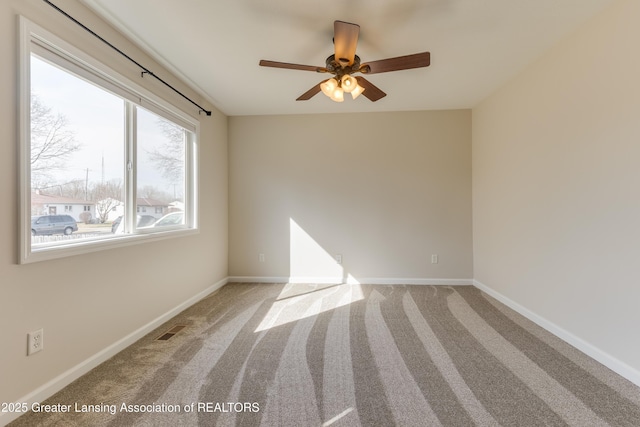 carpeted spare room featuring visible vents, baseboards, and a ceiling fan