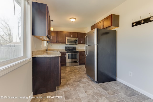 kitchen with baseboards, light countertops, appliances with stainless steel finishes, stone finish floor, and a sink