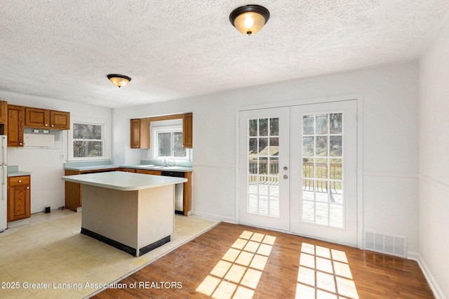 kitchen featuring visible vents, brown cabinets, stainless steel dishwasher, a center island, and light wood finished floors