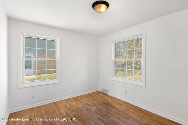 empty room featuring visible vents, a healthy amount of sunlight, baseboards, and wood finished floors