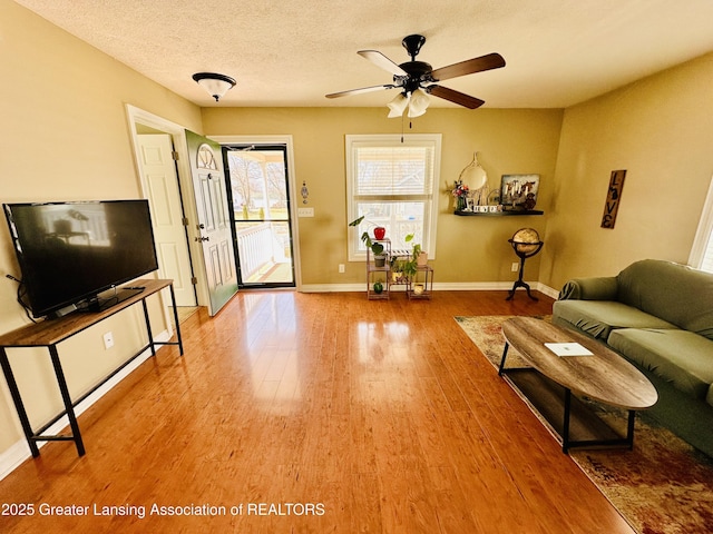 living room featuring baseboards, light wood-style flooring, a textured ceiling, and ceiling fan