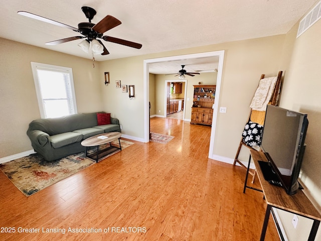 living area with light wood-style flooring, visible vents, and ceiling fan