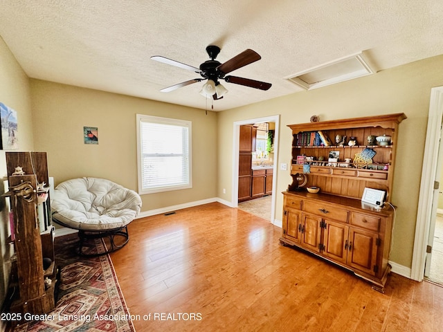 sitting room featuring light wood finished floors, visible vents, ceiling fan, attic access, and a textured ceiling