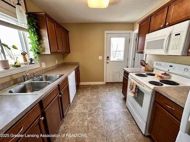 kitchen with brown cabinets, a sink, a textured ceiling, white appliances, and baseboards