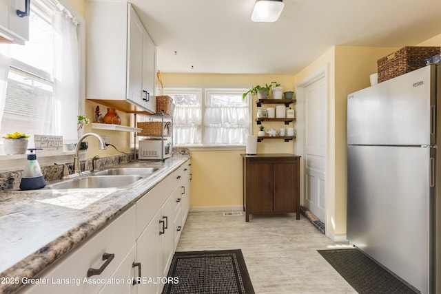 kitchen featuring a sink, open shelves, white cabinets, and freestanding refrigerator