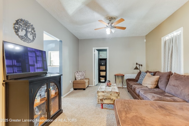 carpeted living room featuring a ceiling fan, baseboards, and a textured ceiling