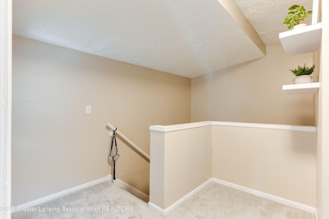 hallway featuring baseboards, an upstairs landing, a textured ceiling, and carpet flooring