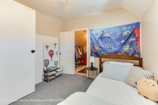 carpeted bedroom with a closet, a textured ceiling, a walk in closet, and lofted ceiling