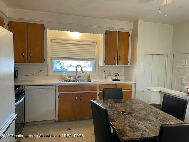 kitchen featuring stainless steel microwave, gas range, brown cabinets, white dishwasher, and a sink