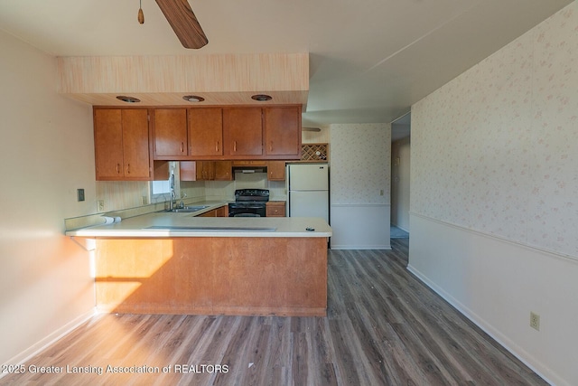 kitchen featuring electric range, a wainscoted wall, freestanding refrigerator, brown cabinetry, and wallpapered walls