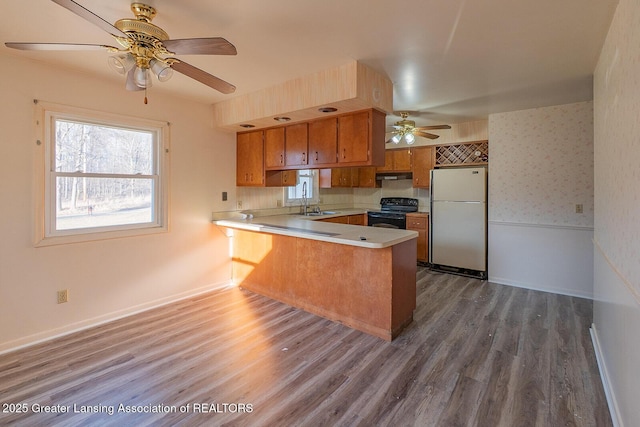 kitchen featuring black range with electric stovetop, brown cabinets, a peninsula, freestanding refrigerator, and a ceiling fan