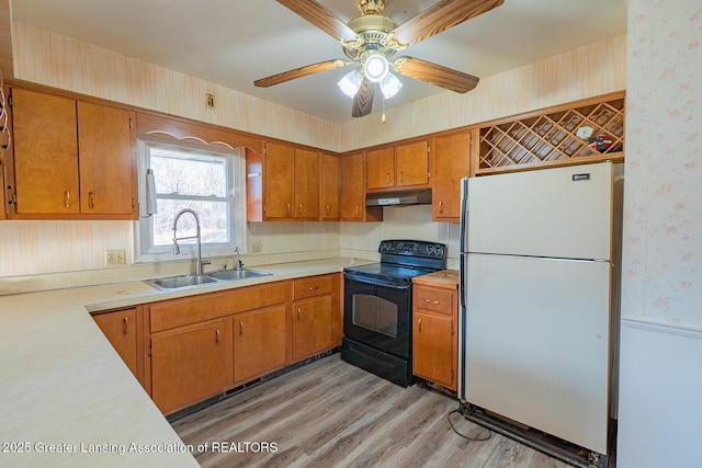 kitchen featuring wallpapered walls, under cabinet range hood, freestanding refrigerator, black / electric stove, and a sink