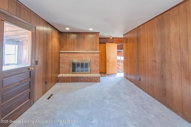 living room with wooden walls, carpet, visible vents, recessed lighting, and a brick fireplace